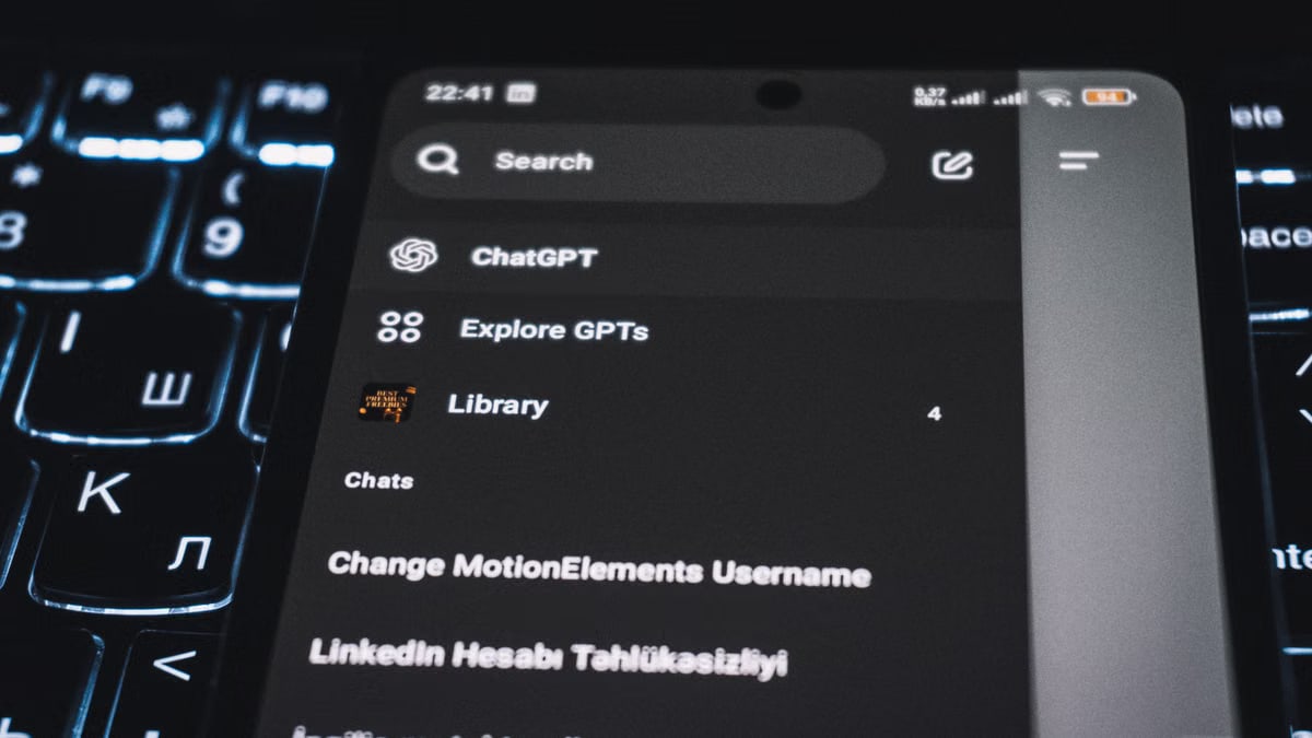 Close-up of a smartphone displaying a chat app interface with a backlit keyboard in the background.